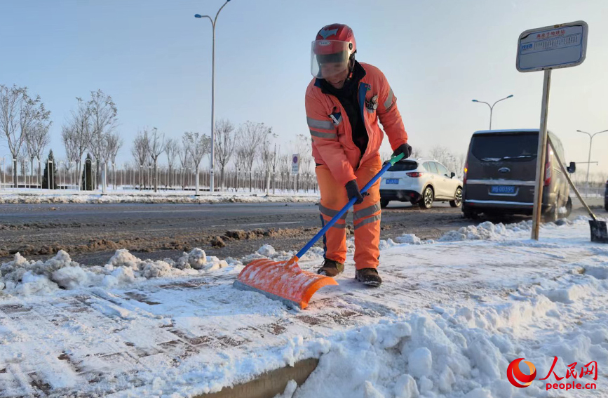 公交站边，环卫工人手持推雪板，为市民扫出“平安路”，创造安全的通行环境。人民网 郭维瑾摄